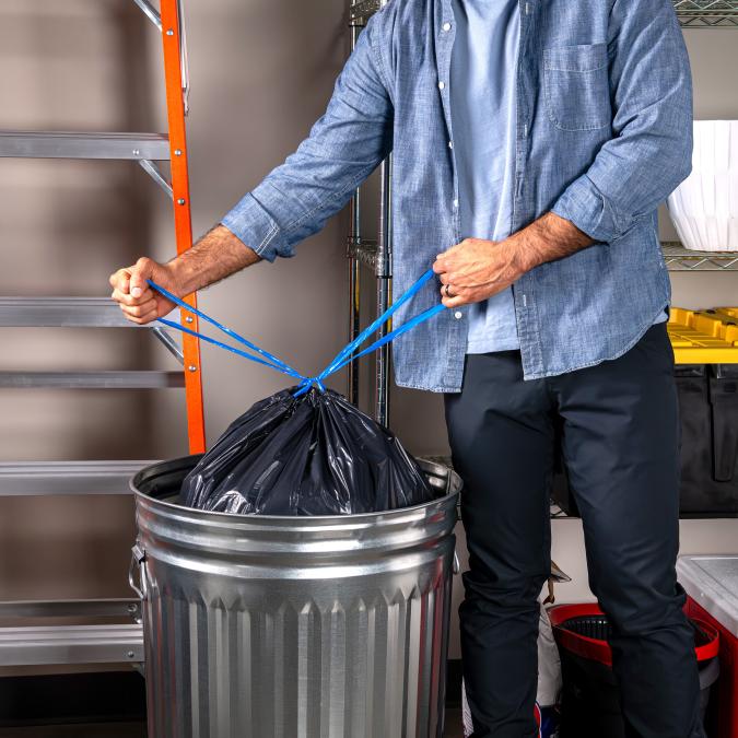 person tying the drawstrings on a 30 gallon Hefty Strong large black trash bag