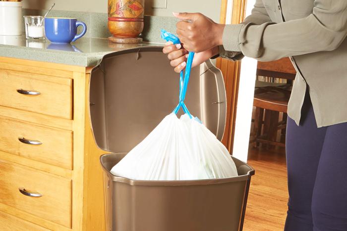 Person pulling a strong drawstring kitchen trash bag out of a trash can.