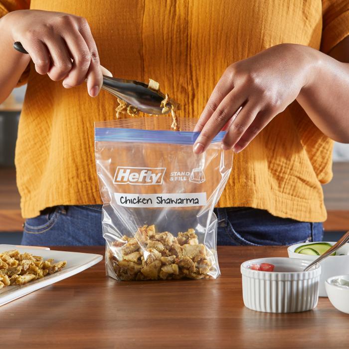 Person filling a quart sized Hefty Press to Close freezer bag with leftover chicken shawarma