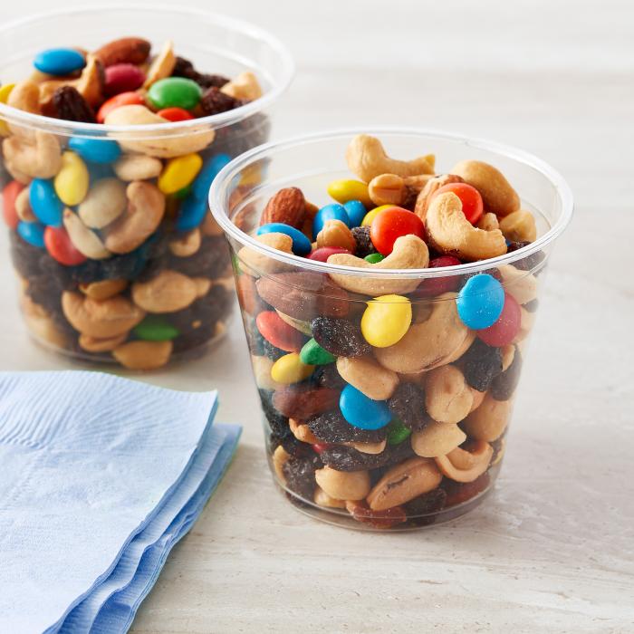 Clear 9oz cup filled with a trail mix of nuts, raisins and m&ms 