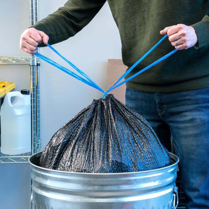 Person tying the drawstrings of a trash bag and pulling it out of the garbage can