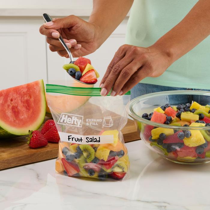 Person scoping fruit salad into a Hefty press to close sandwich bag