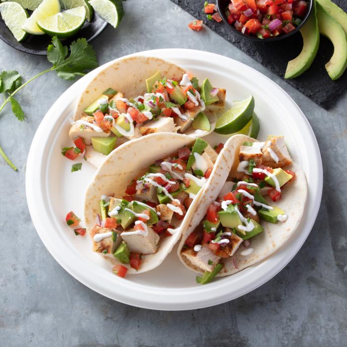 Chicken tacos on a disposable plate on a kitchen counter surrounded by toppings