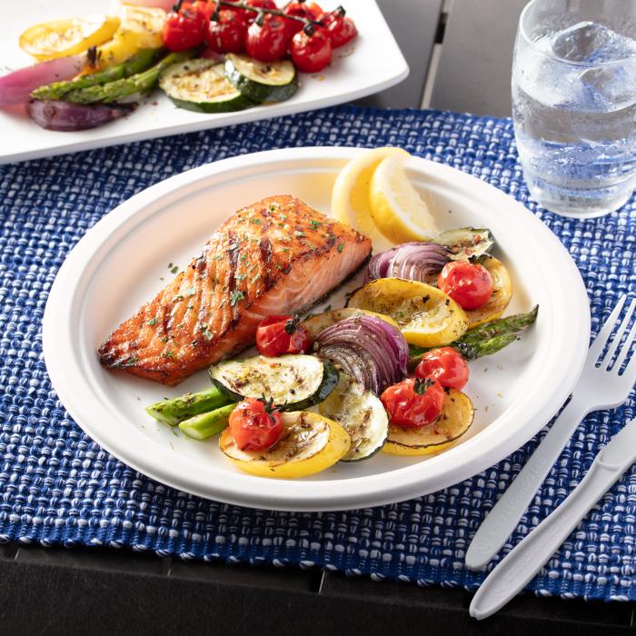 Salmon and roasted vegetables on a disposable plate sitting on an outdoor table