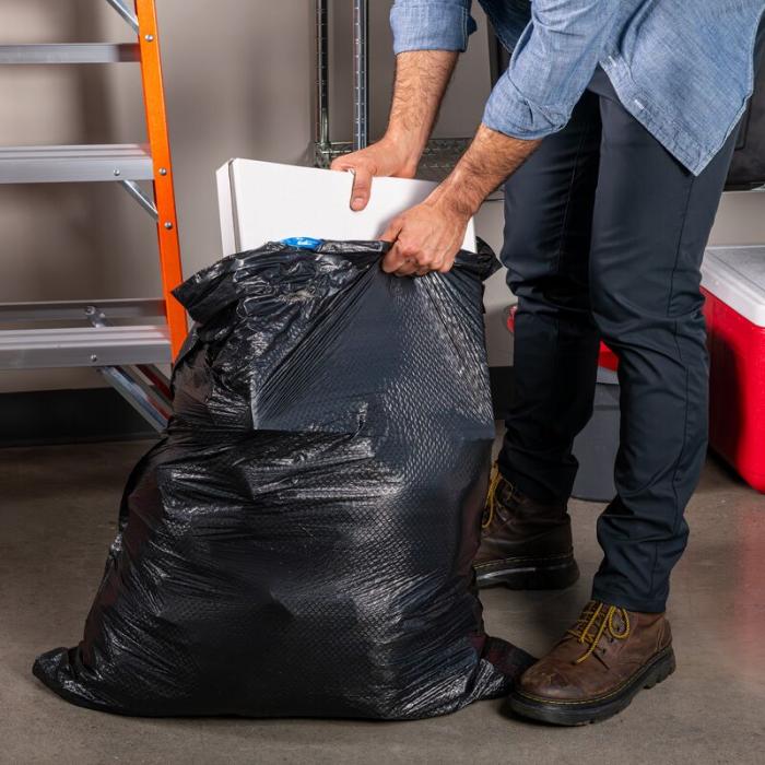 Person putting a large pizza box into a Hefty Ultra Strong large black garbage bag