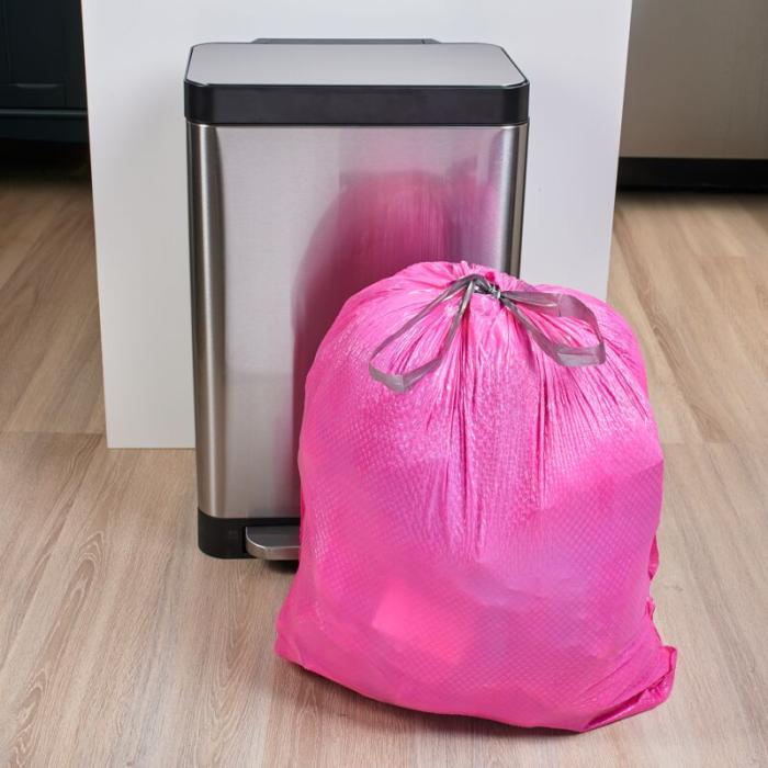 Pink garbage bag tied close with a drawstring and sitting in front of a stainless steal 13 gallon trash can