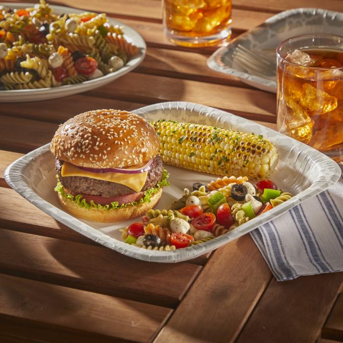 Cheeseburger, corn on the cob and pasta salad on a Hefty Extra Deep paper plate sitting on an outdoor table