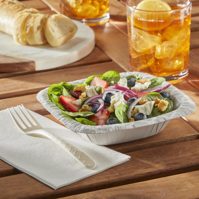 Spinach salad in a Hefty Extra Deep paper bowl alongside a fork and glass of ice tea on an outdoor table