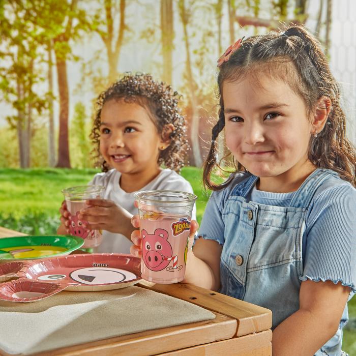 Two girls sitting at an outdoor picnic table drinking pink lemonade