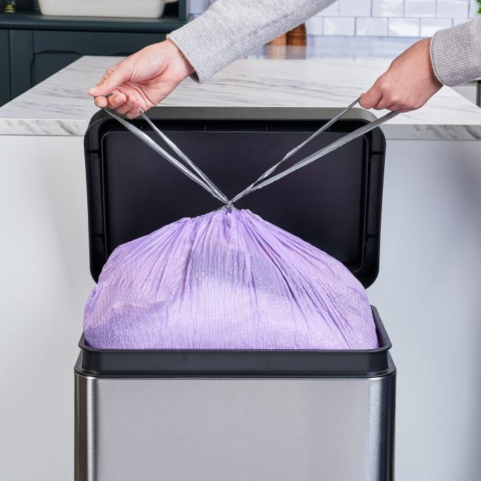 Person tying the drawstrings on a purple Hefty Ultra Strong garbage bag