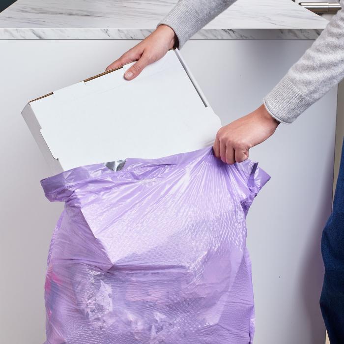 Person putting a large pizza box in a Hefty Ultra Strong Tall Kitchen Purple Trash Bag