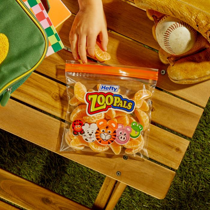 childing removing an orange slices from a Hefty Zoo Pals sandwich bag sitting on an outdoor picnic table