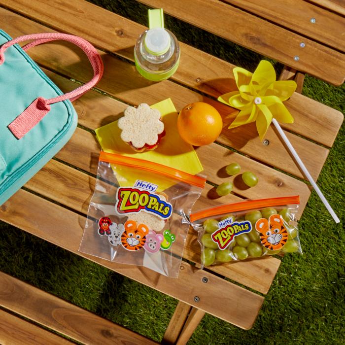 picnic table topped with a lunch box and a sandwich and grapes in Hefty Zoo Pals storage bags