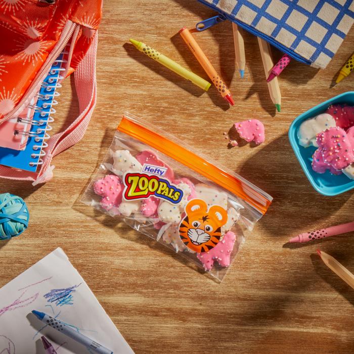 Frosted animal crackers in a Hefty Zoo Pals snack bag sitting on a table alongside a backpack