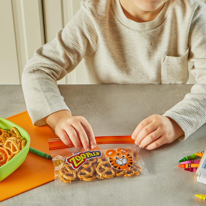 child sealing a Hefty Zoo Pals printed snack bag filled with pretzels