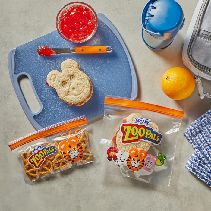 Peanut butter and jelly sandwich sitting on a cutting board alongside a Hefty Zoo Pals storage bag filled with pretzels and a sandwich