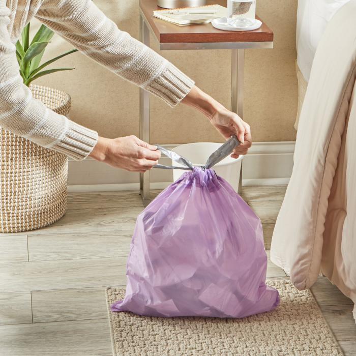 person tying the drawstrings of a small purple colored trash bag