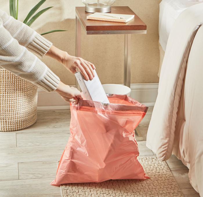 person placing garbage in a small peach colored trash bag