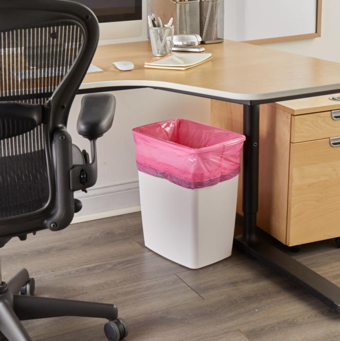 trash can lined with a pink trash bag sitting underneath the desk in an office