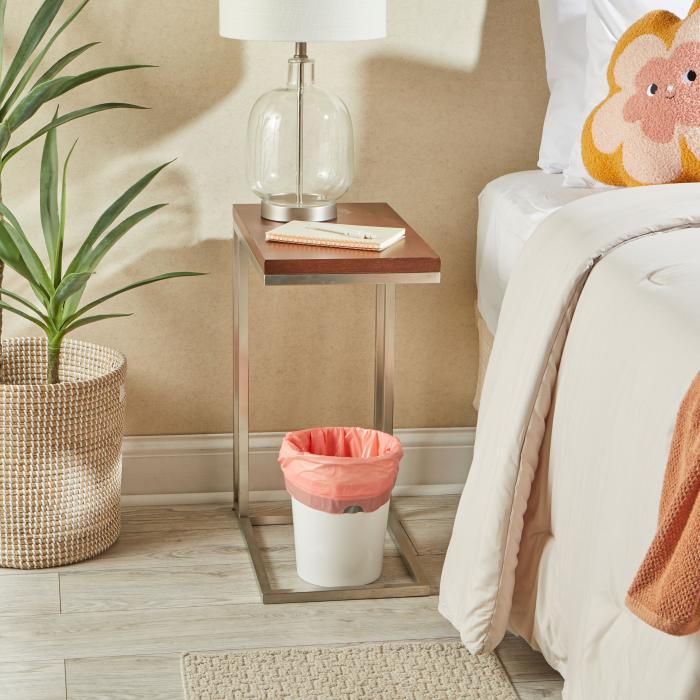 small trash can in a bedroom lined with a peach colored trash bag