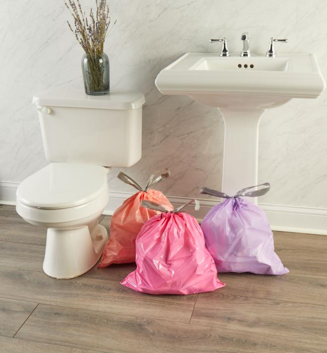 peach, pink and purple small trash bags stuffed and tied sitting on a bathroom floor