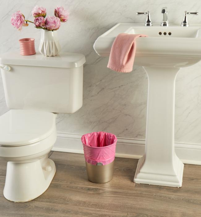 small trash can lined with a pink trash bag sitting in a bathroom next to a toilet and sink