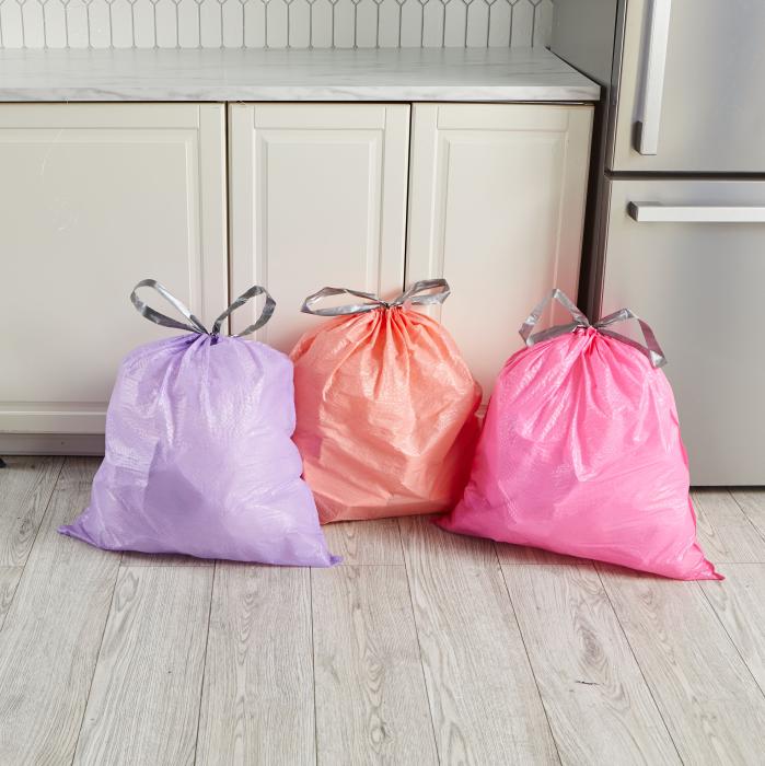 Purple, peach and pink colored Hefty Ultra Strong Color Series trash bags sitting on a kitchen floor