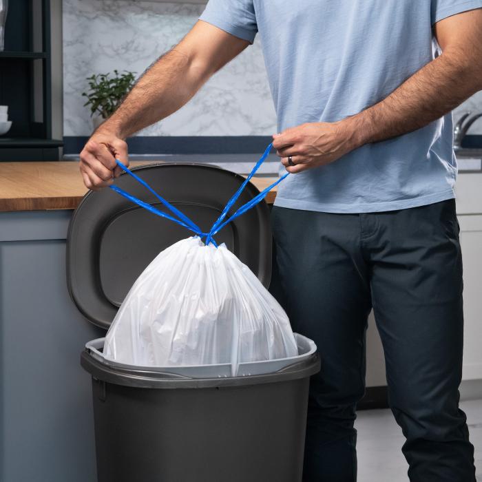 Person tying the drawstring on a Hefty Strong 13 gallon tall kitchen trash bag